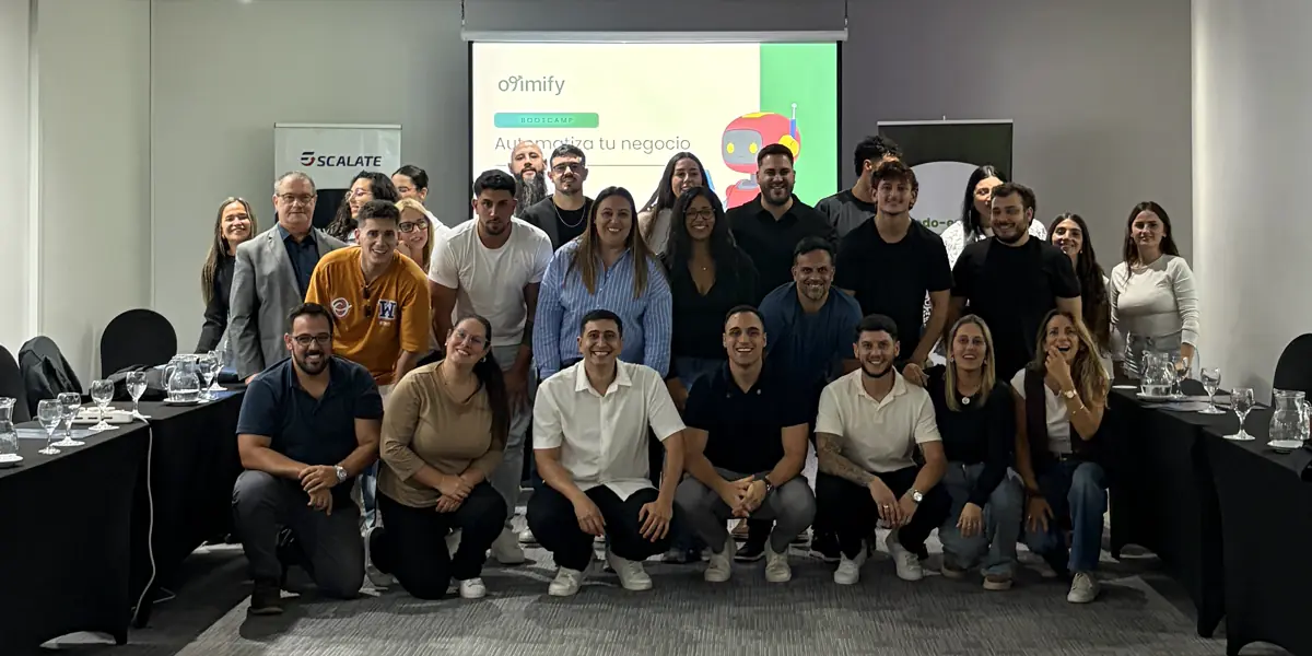 Foto grupal al final del bootcamp, con el logo de Otimify y el título “Automatiza tu negocio” proyectados en la pantalla y un banner de Escalate a un costado.